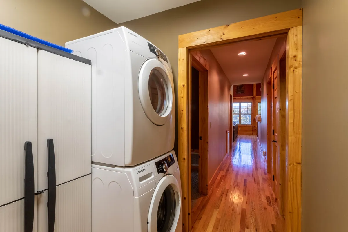 This image presents a practical and welcoming area with a stacked washer and dryer, a laundry storage unit, and a hallway leading toward the living space. The scene suggests an area easily accessible for guests and their pets after outdoor adventures.
