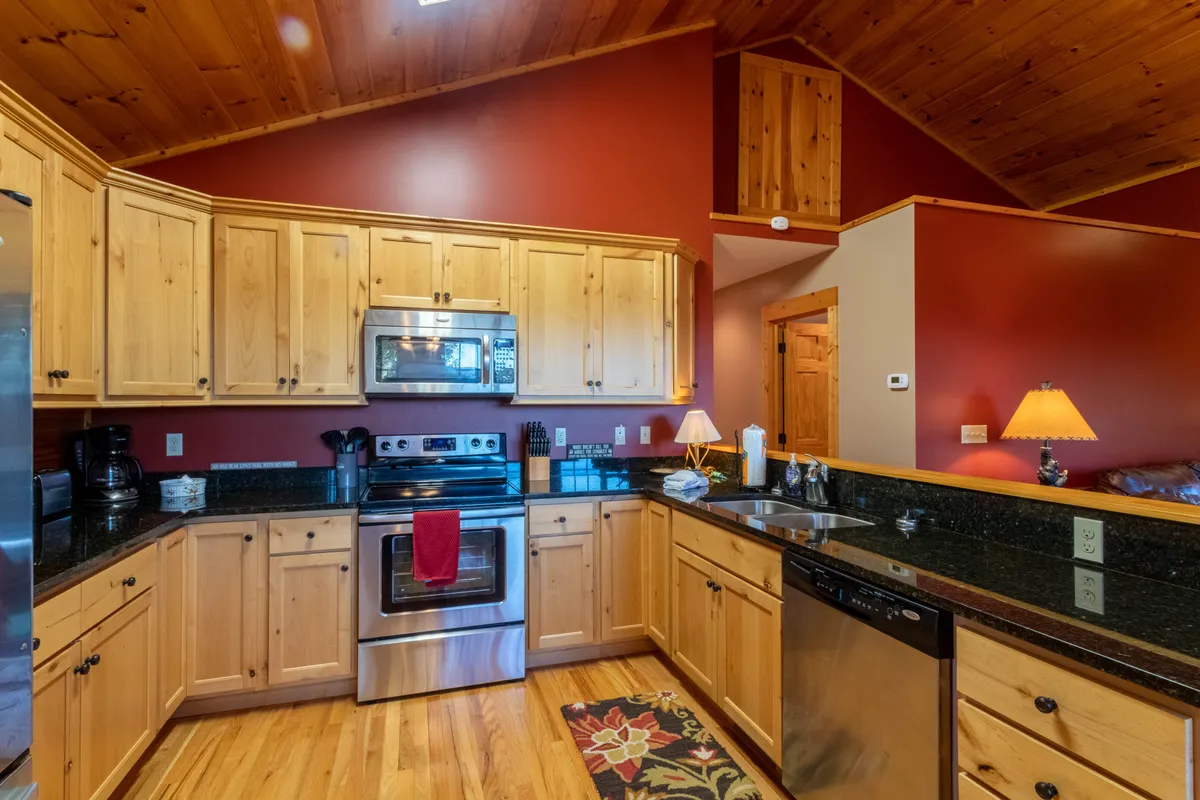 A cozy and welcoming kitchen featuring warm wooden cabinetry, sleek black granite countertops, and modern appliances. The space feels inviting and is ideal for relaxing with loved ones after a day outside.