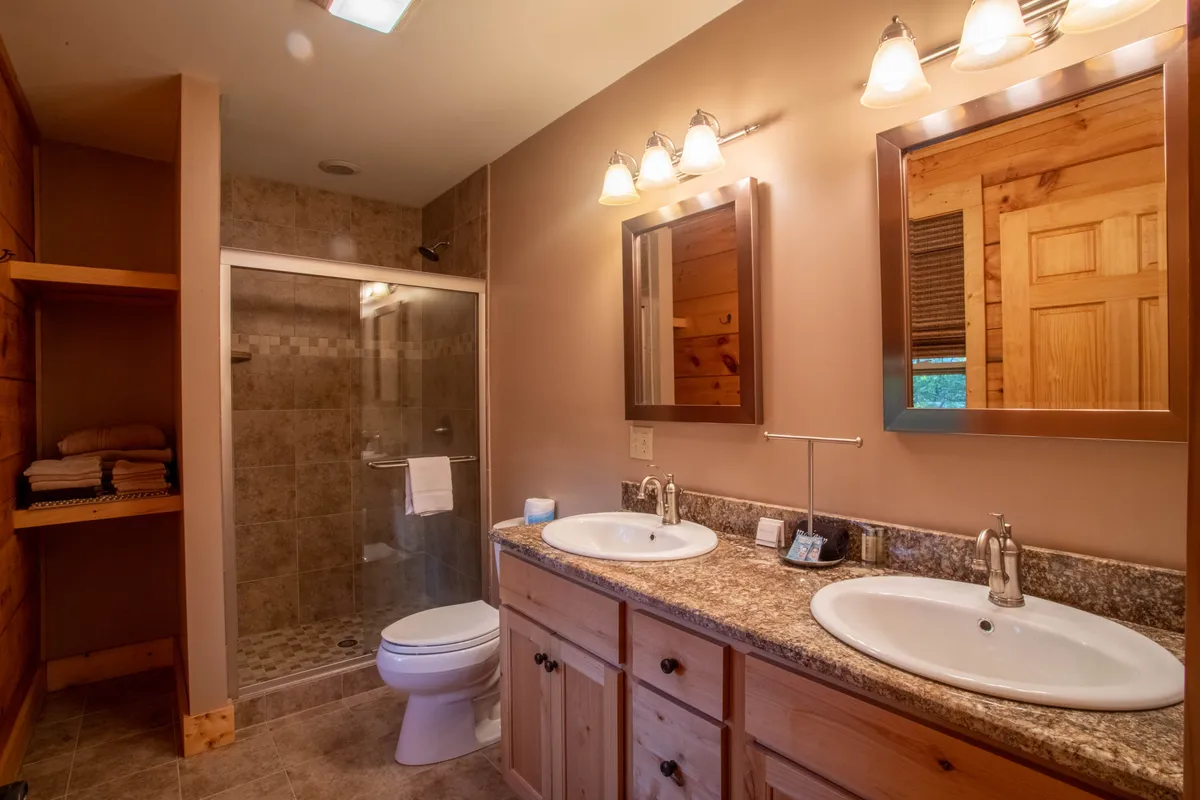 A modern bathroom space with double sinks, mirrors, a shower area, and wooden cabinetry. The serene, inviting mood is ideal for self-care routines and relaxation after a day of adventure.