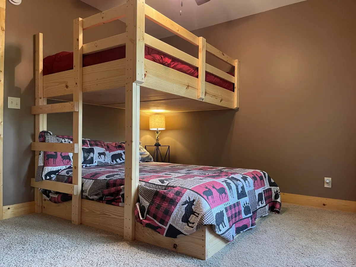 The photo showcases a full-over-queen bunk bed with a charming bedspread featuring animal patterns, complemented by a bedside lamp, creating a warm and playful environment perfect for families or groups.