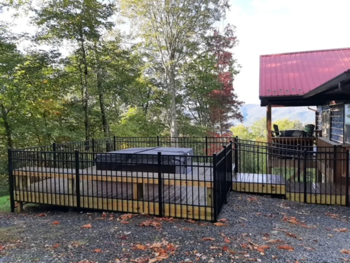 This exterior shot captures the wooden deck with the hot tub, set amidst lush trees and offering a distant mountain view. The scene is peaceful and inviting, with the hot tub positioned to take in sunset or nighttime stargazing. It also hints at social gatherings with space for guests to relax and enjoy nature.